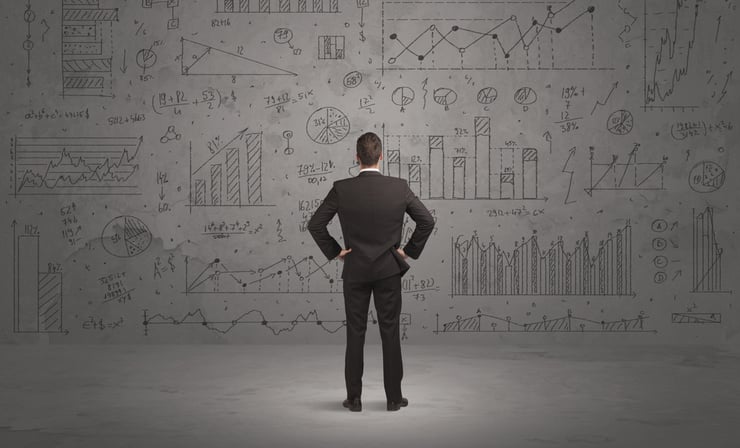 A successful confident businessman thinking about decisions, standing in front of wall full with graph pie charts and calculations concept