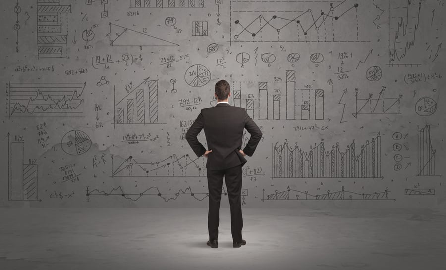 A successful confident businessman thinking about decisions, standing in front of wall full with graph pie charts and calculations concept